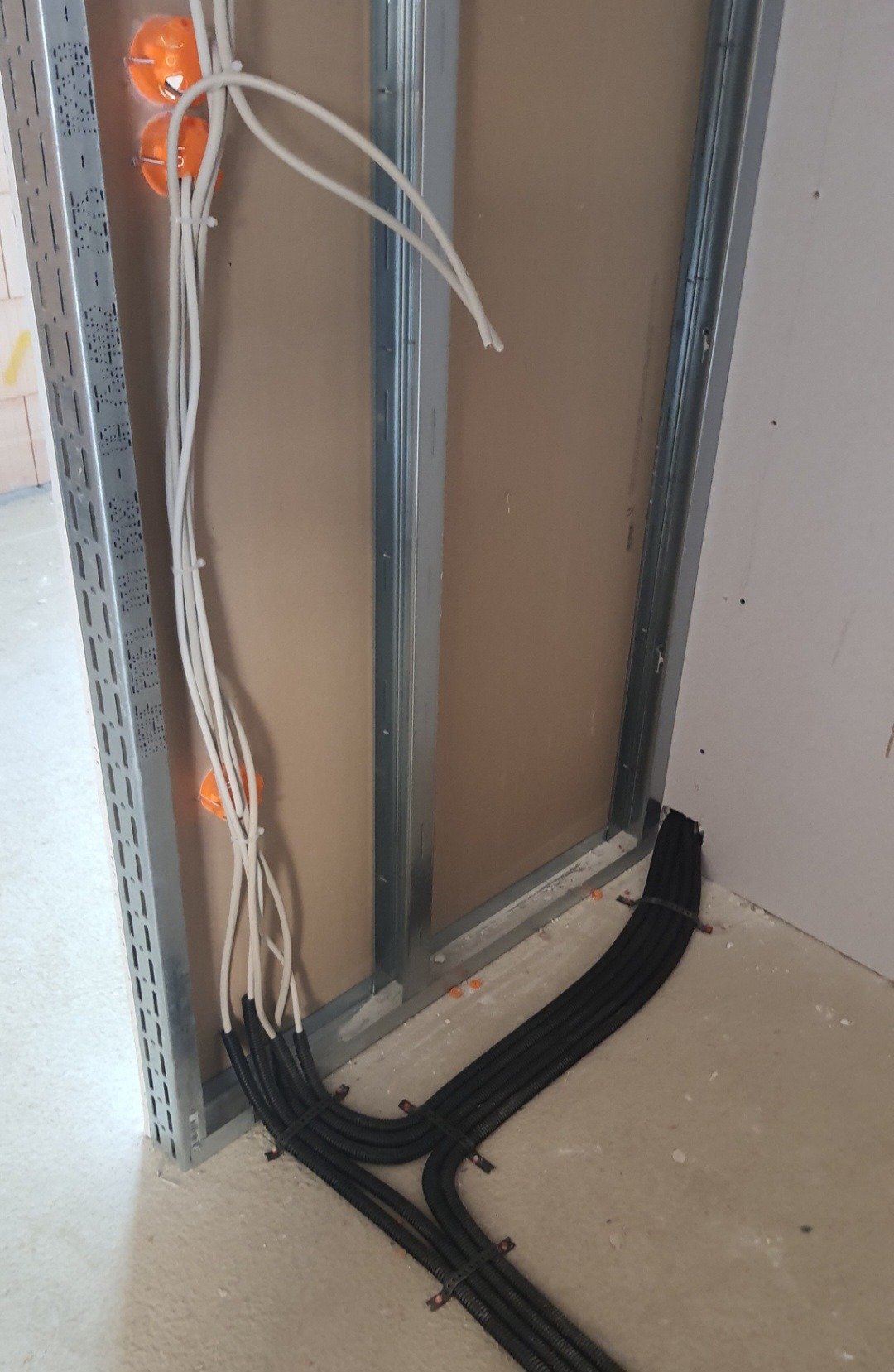 Kable elektryczne w peszlach prowadzone wzdłuż metalowej konstrukcji ściany działowej, widoczne pomarańczowe puszki instalacyjne.