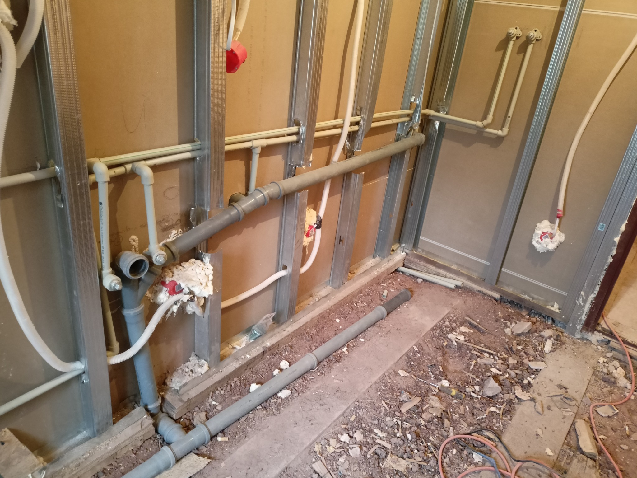 Wnętrze w trakcie remontu z widocznymi rurami instalacji wodnej i kanalizacyjnej, zamocowanymi do metalowej konstrukcji ścian działowych, częściowo uszczelnionymi pianką montażową, na podłodze gruz...