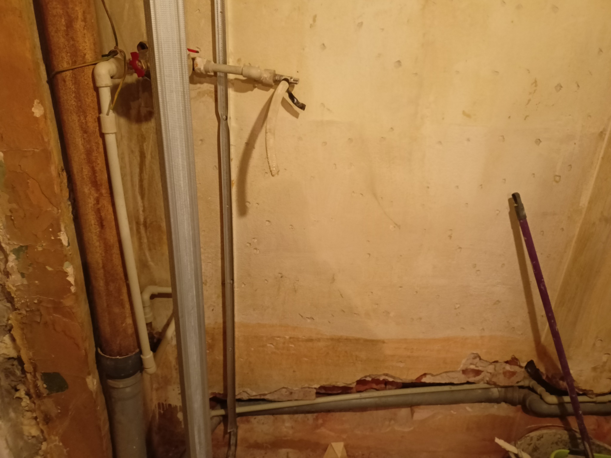 Fragment ściany w trakcie remontu z widocznymi rurami hydraulicznymi, metalowym profilem i śladami po starej instalacji.