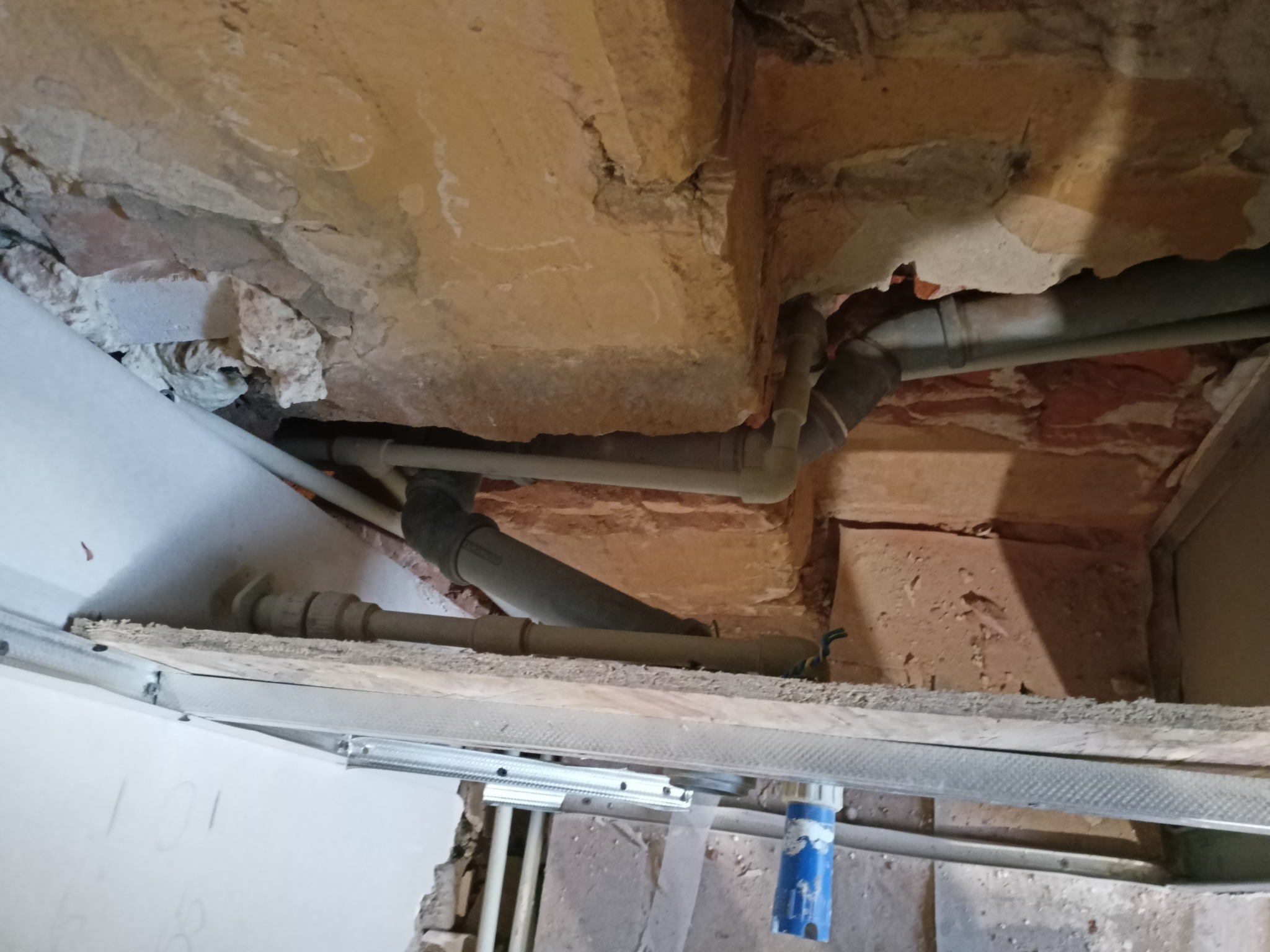 Rury kanalizacyjne pod sufitem w trakcie prac remontowych, widoczne elementy konstrukcyjne sufitu podwieszanego.