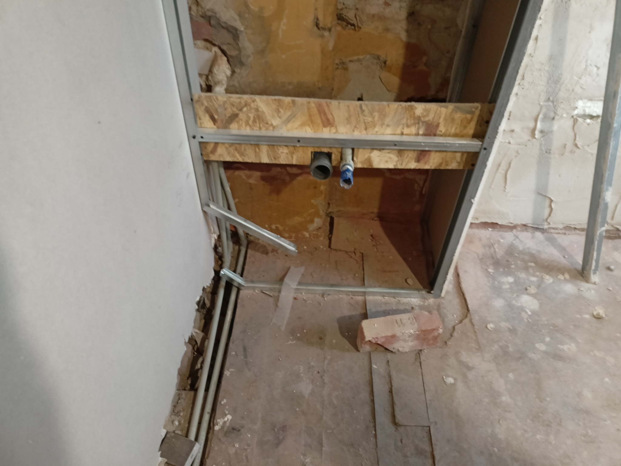 Wnętrze ściany w trakcie remontu z widocznymi rurami instalacji wodnej zamontowanymi na drewnianej konstrukcji i metalowych profilach.