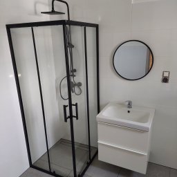 PAMIREX REMONTY I WYKONCZENIA PAWEŁ HAWRO - Nowoczesna łazienka z kabiną prysznicową typu walk-in z czarnymi profilami, białą umywalką z szafką i okrągłym lustrem na białych płytkach.