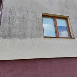 PAMIREX REMONTY I WYKONCZENIA PAWEŁ HAWRO - Fragment ściany budynku z widocznym zabrudzeniem elewacji przed czyszczeniem, okna z brązowymi ramami, dolna część ściany w kolorze bordowym.