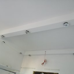 PAMIREX REMONTY I WYKONCZENIA PAWEŁ HAWRO - Biały sufit podwieszany z wbudowanymi okrągłymi lampami LED, widoczne przewody elektryczne zwisające ze ściany wskazujące na trwające prace instalacyjne.