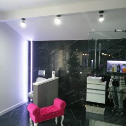 PAMIREX REMONTY I WYKONCZENIA PAWEŁ HAWRO - Nowoczesna łazienka z czarnymi marmurowymi płytkami, podświetleniem LED, białą umywalką z szafką i różową pufą na białych nóżkach.