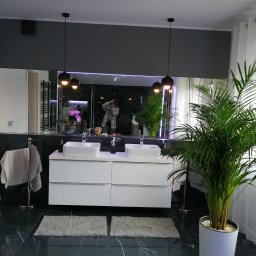 PAMIREX REMONTY I WYKONCZENIA PAWEŁ HAWRO - Nowoczesna łazienka z podwójną umywalką nablatową na białej szafce, czarne płytki podłogowe z białymi żyłami, duże lustro z odbiciem osoby robiącej zdjęcie, wiszące czarne lampy i roślina...