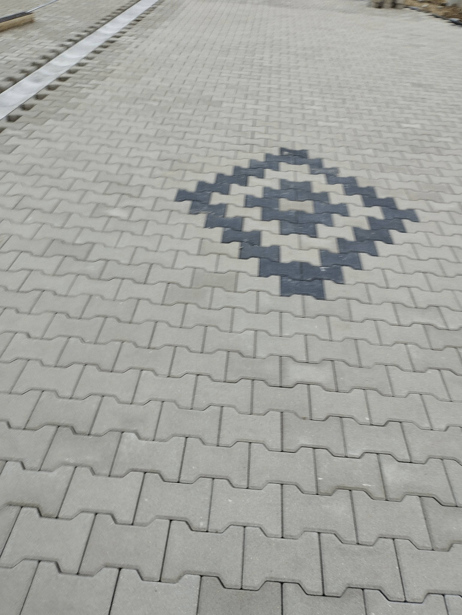 Ułożona szara kostka brukowa typu 'I' z ciemnoszarym wzorem rombu w centralnej części, widok z góry pod kątem.