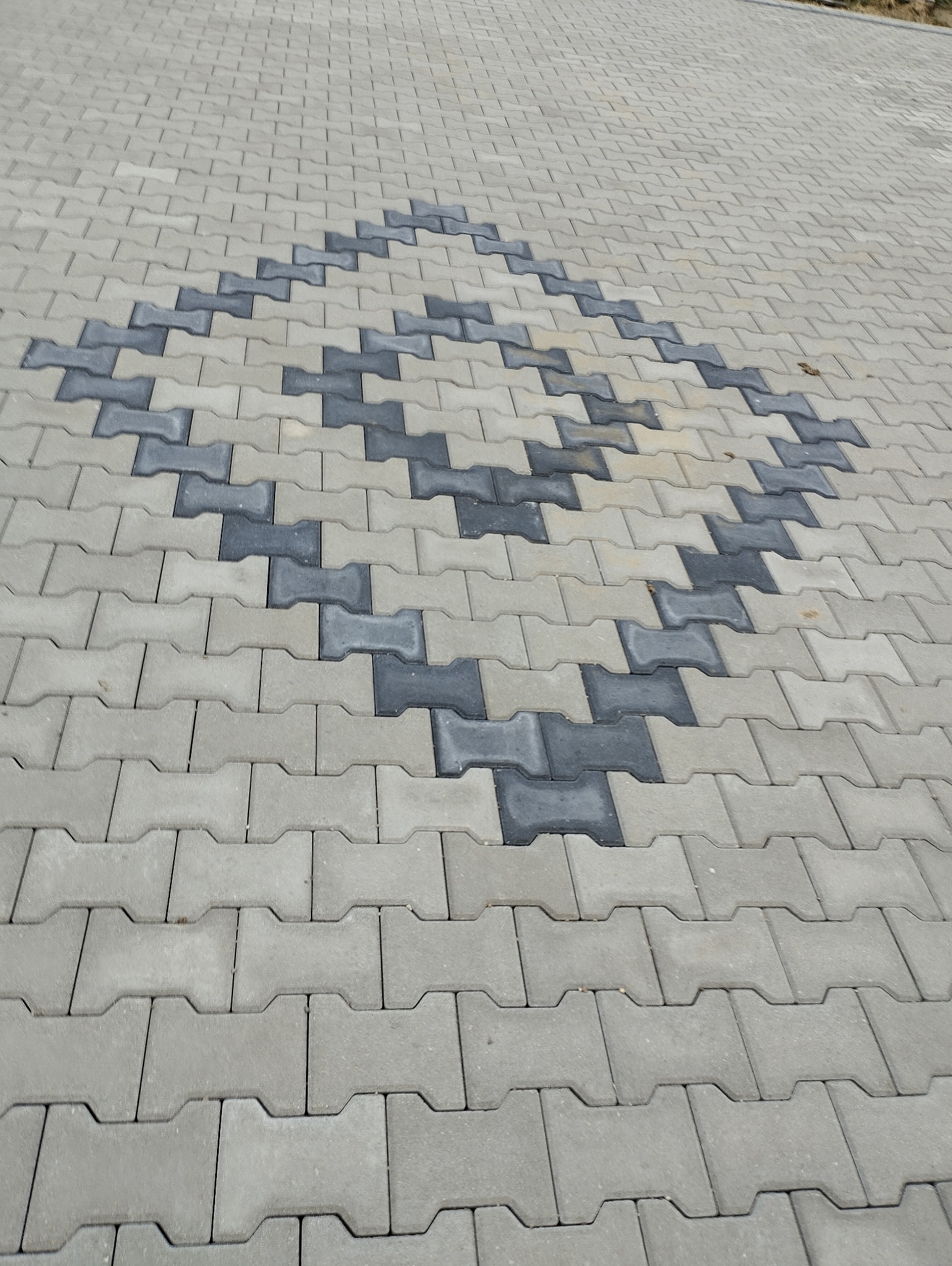 Ułożona kostka brukowa typu 'H' w dwóch odcieniach szarości tworząca wzór rombu.