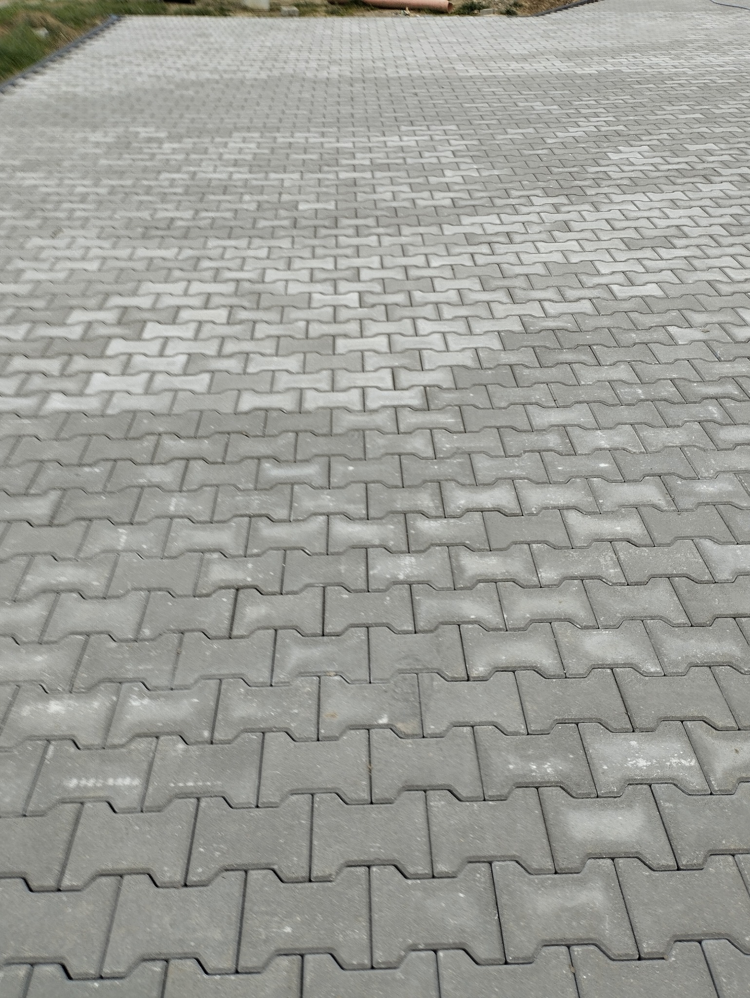 Szara kostka brukowa ułożona w wzór jodełki, widoczna z perspektywy lekko z góry, z delikatnym gradientem wilgoci na niektórych kostkach.