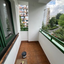 Ruslan Sobolivskyi - Świeżo pomalowany balkon z widokiem na budynki mieszkalne i zieleń, widoczne narzędzia malarskie: puszki z farbą, pędzel i wiadro.