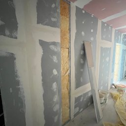 Ruslan Sobolivskyi - Wnętrze w trakcie montażu płyt kartonowo-gipsowych, widoczne profile, izolacja oraz wstępnie zaszpachlowane łączenia płyt na ścianach i suficie, narzędzia i wiaderka na podłodze.