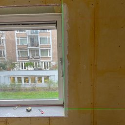 Ruslan Sobolivskyi - Montaż płyty karton gips przy oknie z widocznym laserem poziomującym, taśmą mierniczą i nożykiem na parapecie.