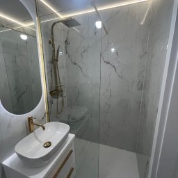 Ruslan Sobolivskyi - Nowoczesna łazienka z kabiną prysznicową typu walk-in, umywalką nablatową na szafce i podświetlanym lustrem w złotej ramie. Marmurowe płytki na ścianach i oświetlenie LED.