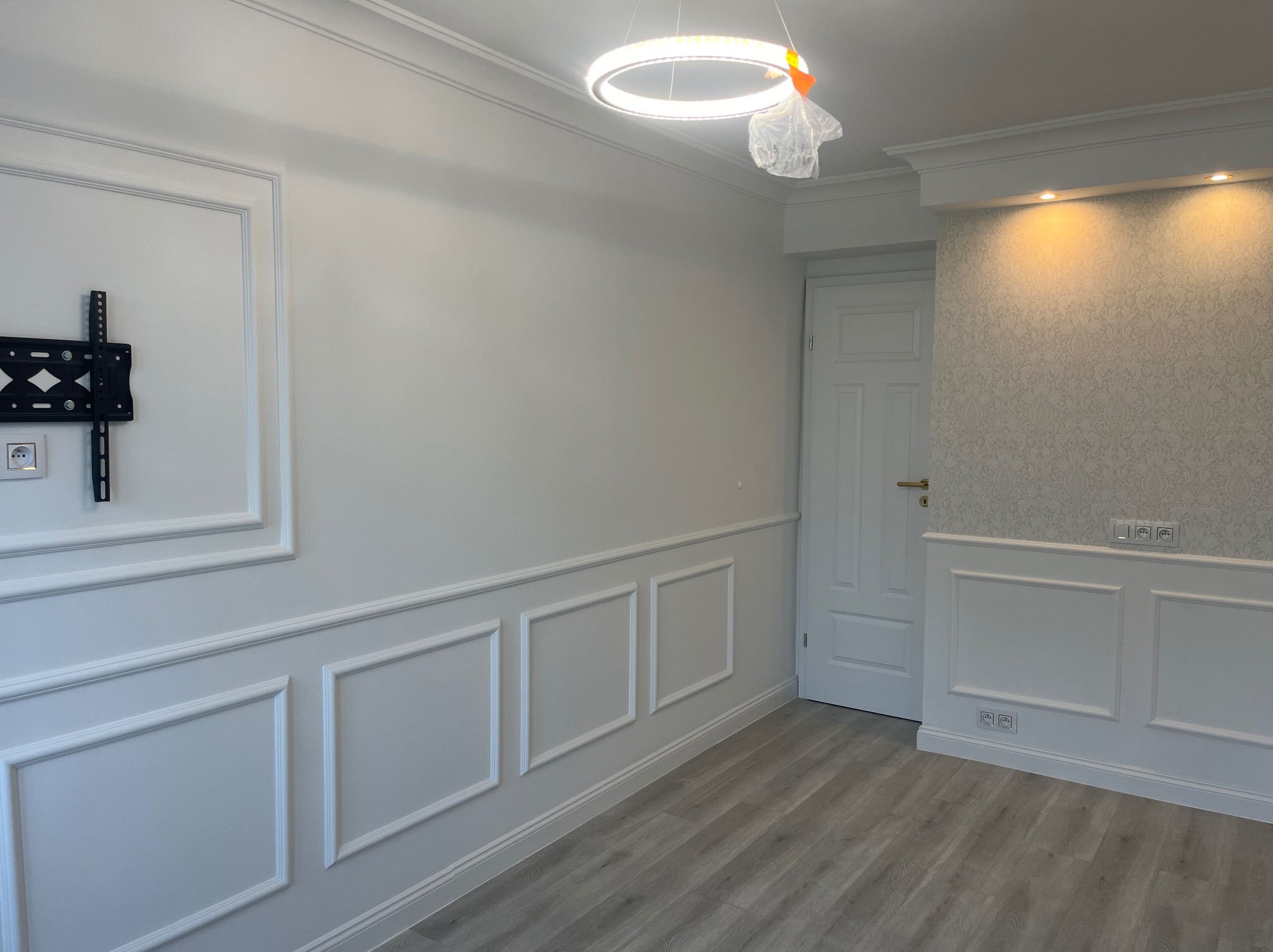 Eleganckie wykończenie wnętrza z białymi panelami ściennymi, dekoracyjną tapetą, nowoczesnym oświetleniem i uchwytem na telewizor. Jasne, stylowe wnętrze.