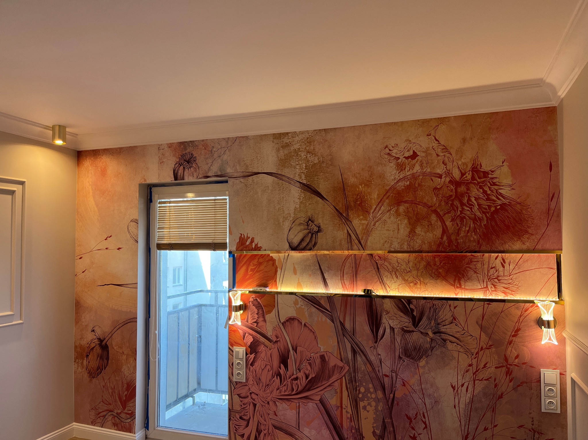 Ściana z dekoracyjną tapetą w kwiaty, podświetlane półki szklane z oświetleniem LED, okno balkonowe z żaluzjami. Wykończone wnętrze pokoju.