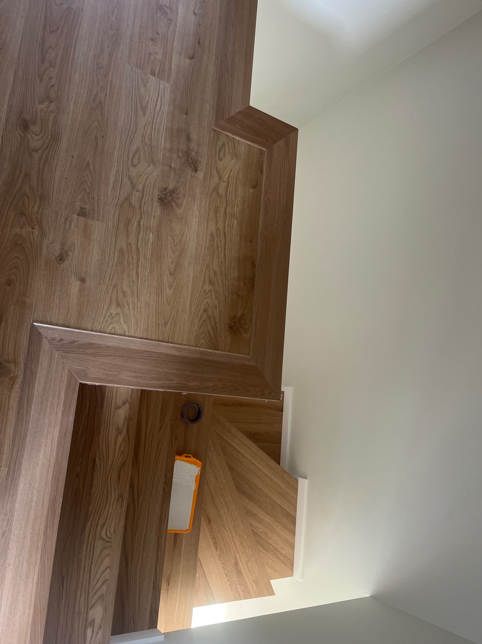 Ukończone schody z drewnianymi panelami, widok z góry. Na podłodze leży wałek malarski i taśma malarska. Ściany pomalowane na biało.