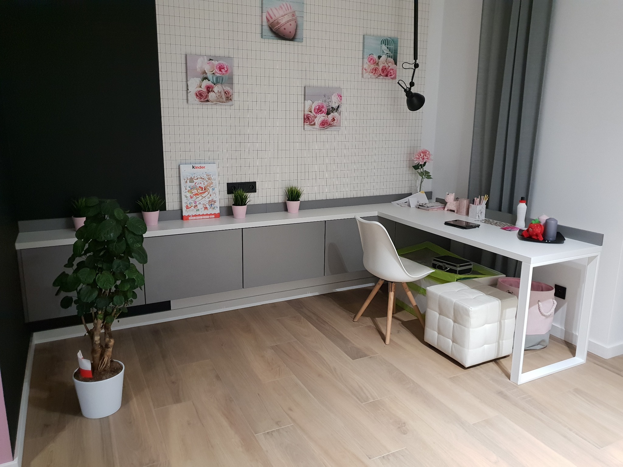 Pokój z szarą zabudową meblową pod ścianą, białym biurkiem i krzesłem, dekoracjami ściennymi w pastelowych kolorach i drewnianą podłogą.