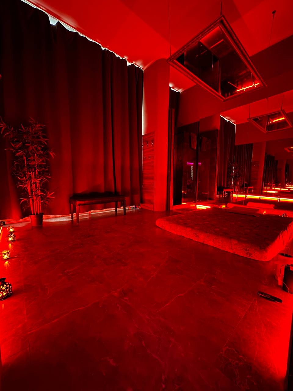 Wnętrze gabinetu z czerwonym oświetleniem, dekoracyjnymi lampionami, lustrami na suficie i niskim łóżkiem.