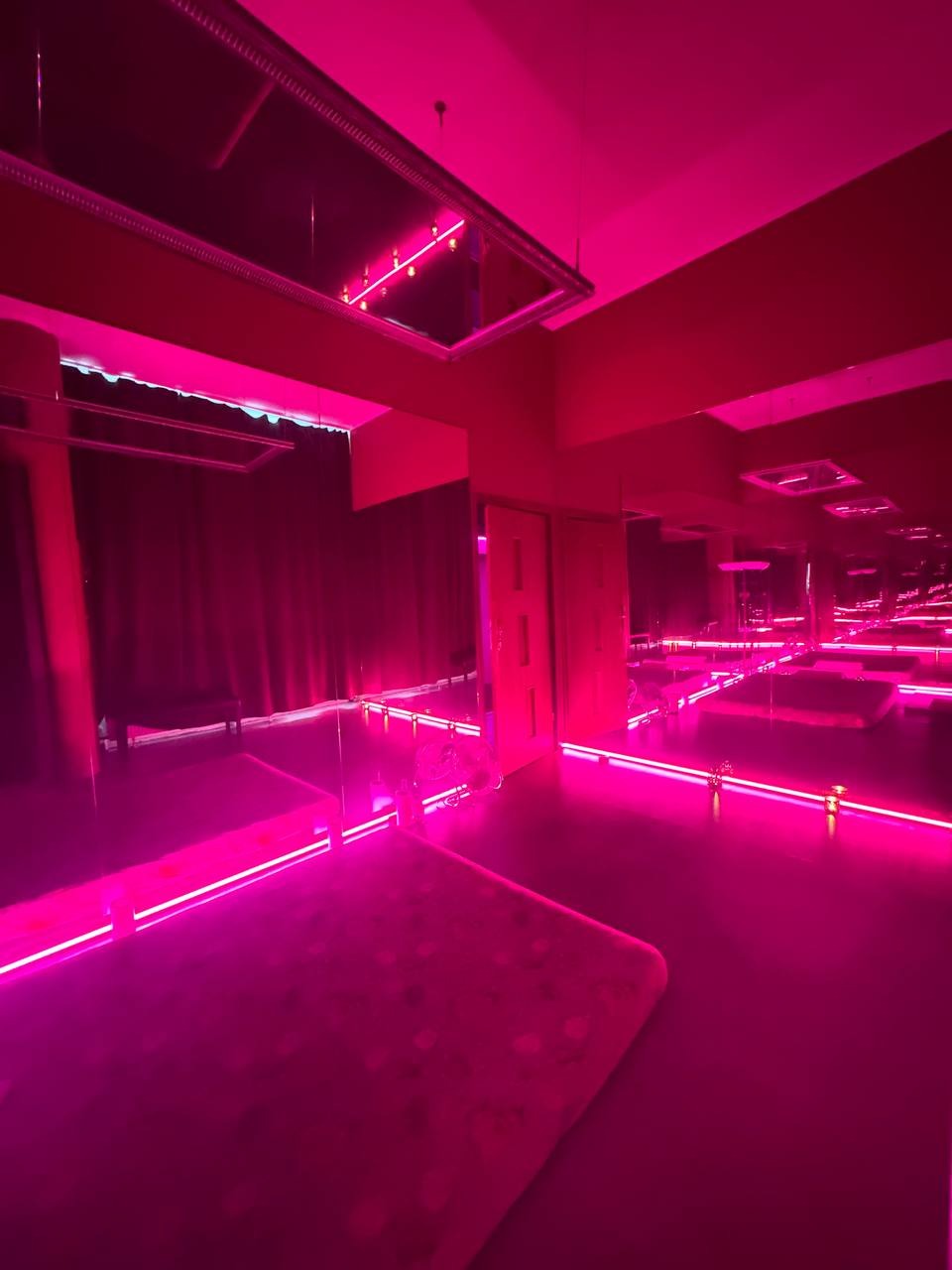 Pokój do zabiegów z podświetlonymi platformami i lustrami w intensywnym różowym oświetleniu.