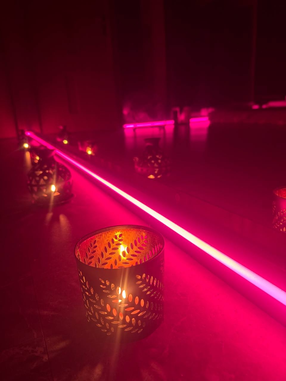 Świece w metalowych lampionach ze wzorem liści i neonowe oświetlenie w odcieniach różu tworzą relaksującą atmosferę w gabinecie.