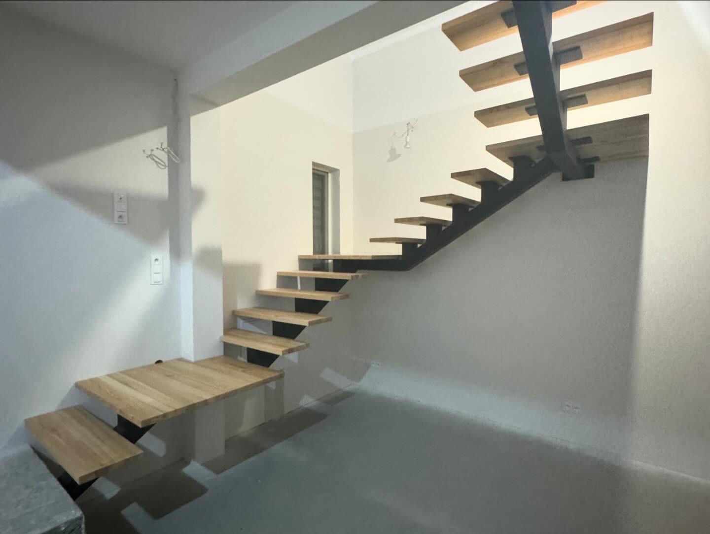 Minimalistyczne schody metalowe z drewnianymi stopniami, wspornik środkowy, surowe wnętrze w trakcie wykończenia.