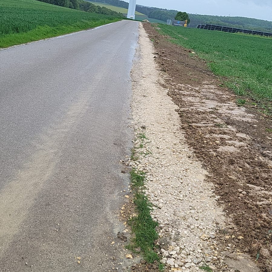 Przygotowanie podłoża obok asfaltowej drogi, wysypany żwir, w tle turbina wiatrowa i panele słoneczne.