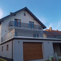 Nowoczesny dom z szarymi balustradami balkonowymi o poziomym układzie szczebli i brązową bramą garażową, widziany z niskiego kąta.