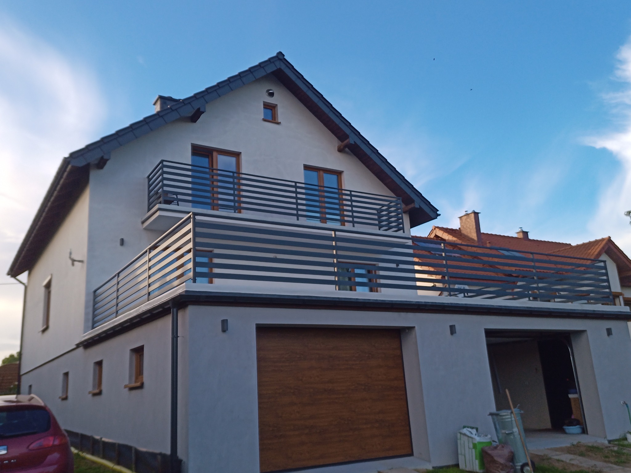 Nowoczesny dom z szarymi balustradami balkonowymi o poziomym układzie szczebli i brązową bramą garażową, widziany z niskiego kąta.
