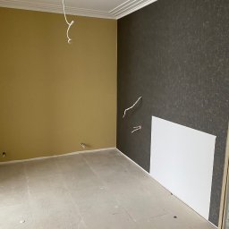 DNIPRO-VOLA SPÓŁKA Z OGRANICZONĄ ODPOWIEDZIALNOŚCIĄ - Pokój po remoncie: ściana w odcieniach brązu z fakturą, druga w kolorze musztardowym, biały sufit z dekoracyjną listwą. Widoczne wystające kable.