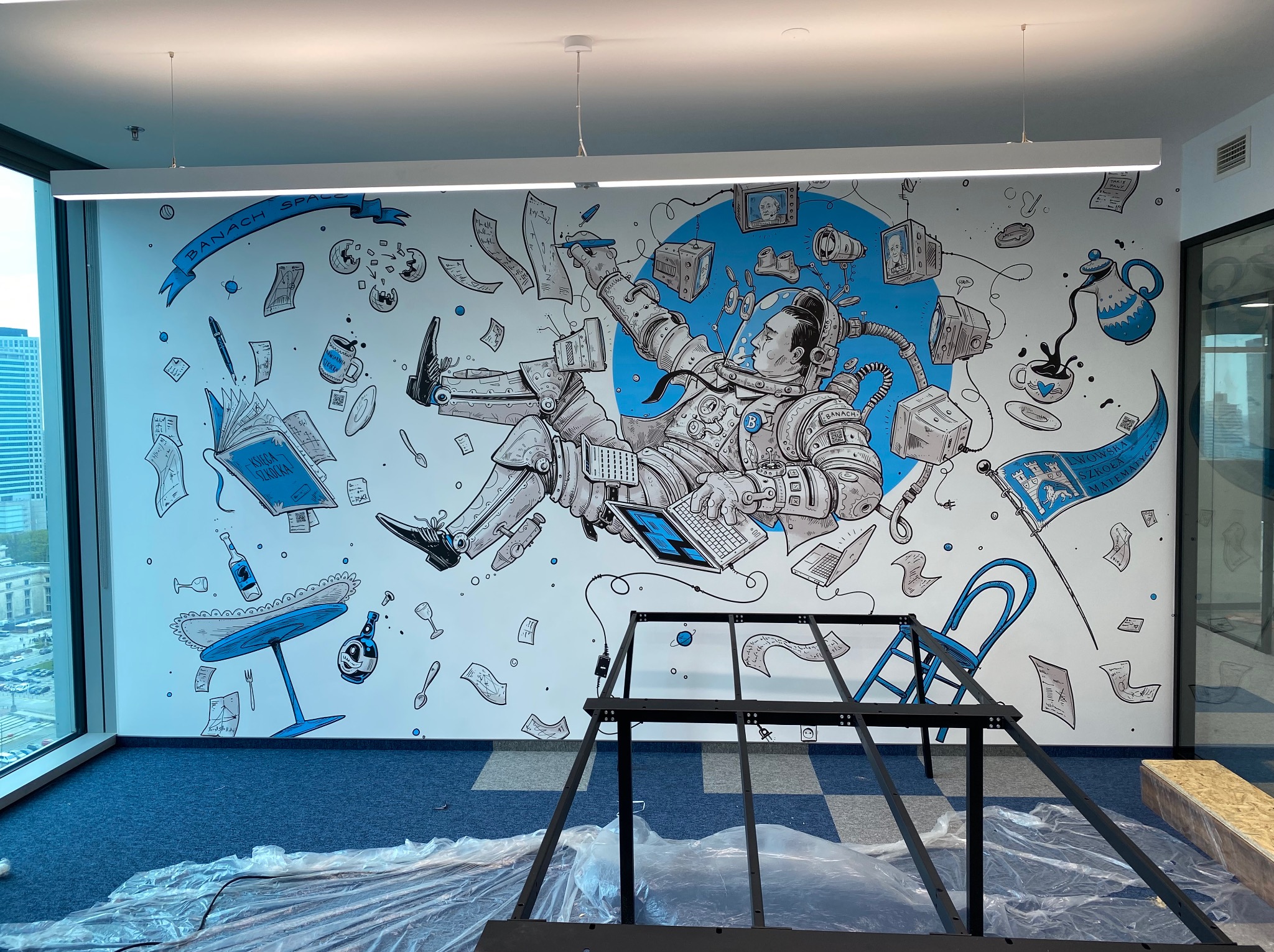 Ręcznie malowana fototapeta w biurze: astronauta w przestrzeni kosmicznej, elementy graficzne w stylu retro, niebieskie akcenty. Widoczny fragment metalowej konstrukcji.