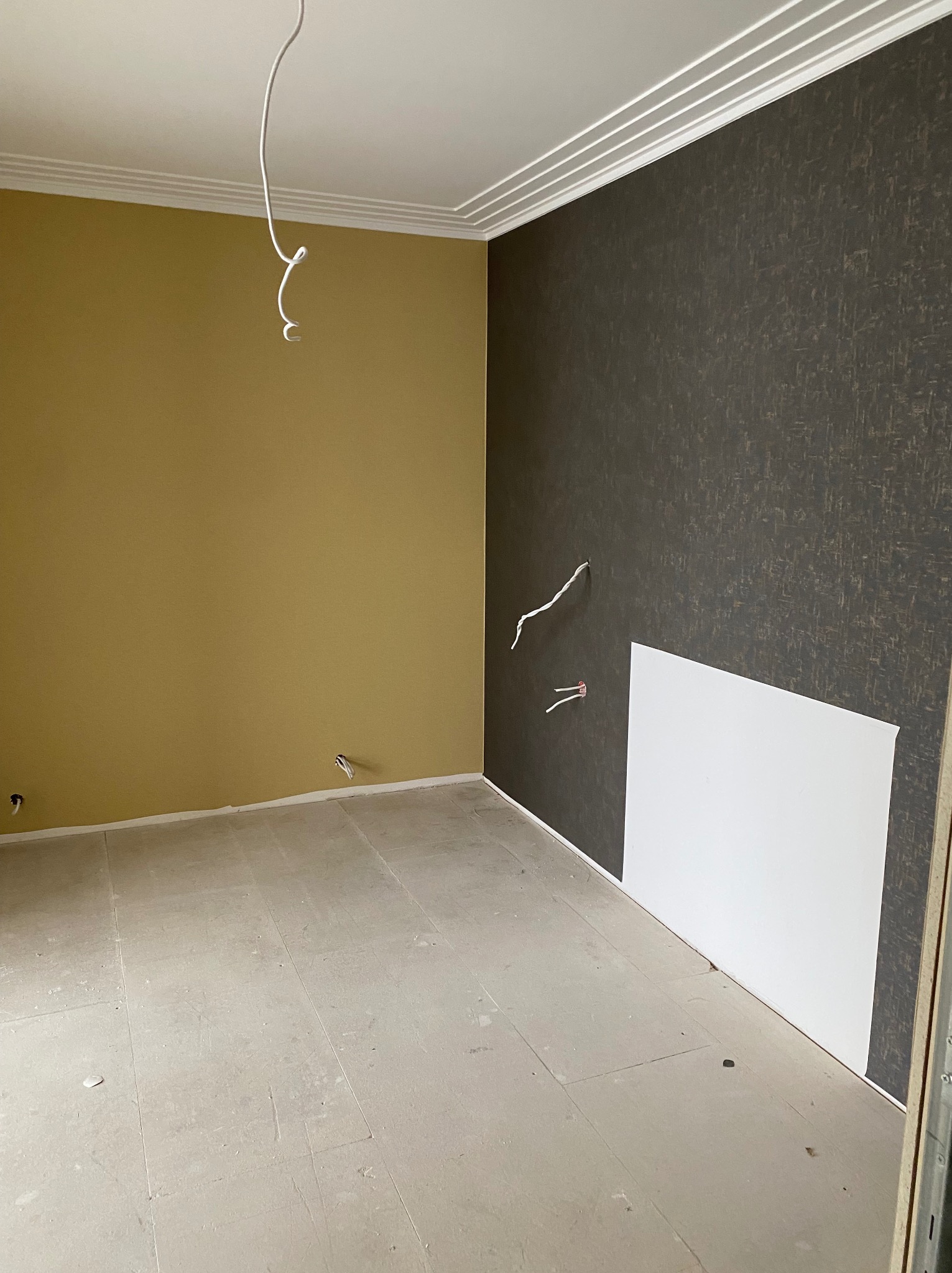 Pokój po remoncie: ściana w odcieniach brązu z fakturą, druga w kolorze musztardowym, biały sufit z dekoracyjną listwą. Widoczne wystające kable.