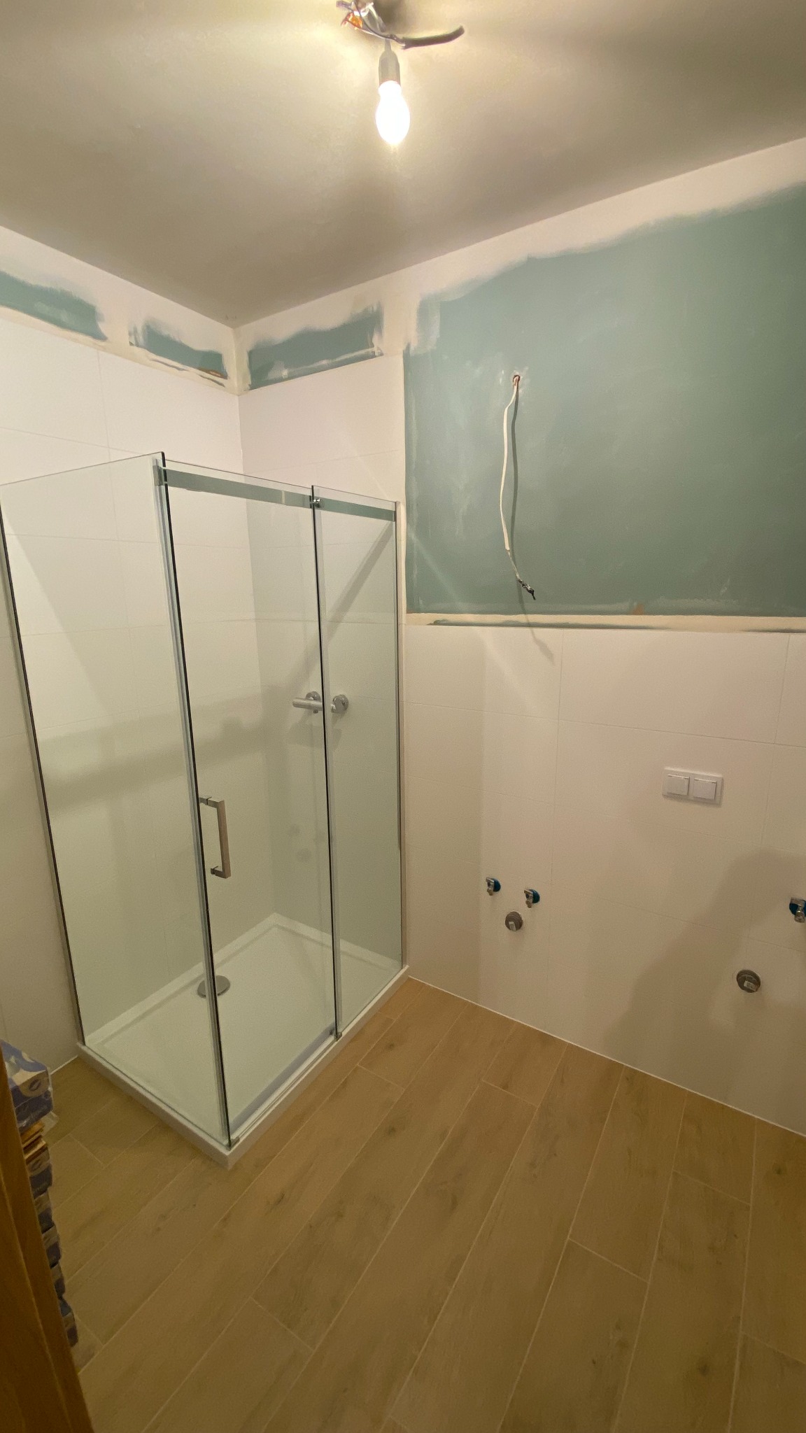 Montaż kabiny prysznicowej w trakcie wykończenia łazienki, widoczne niezakończone malowanie ścian i wystające przewody.