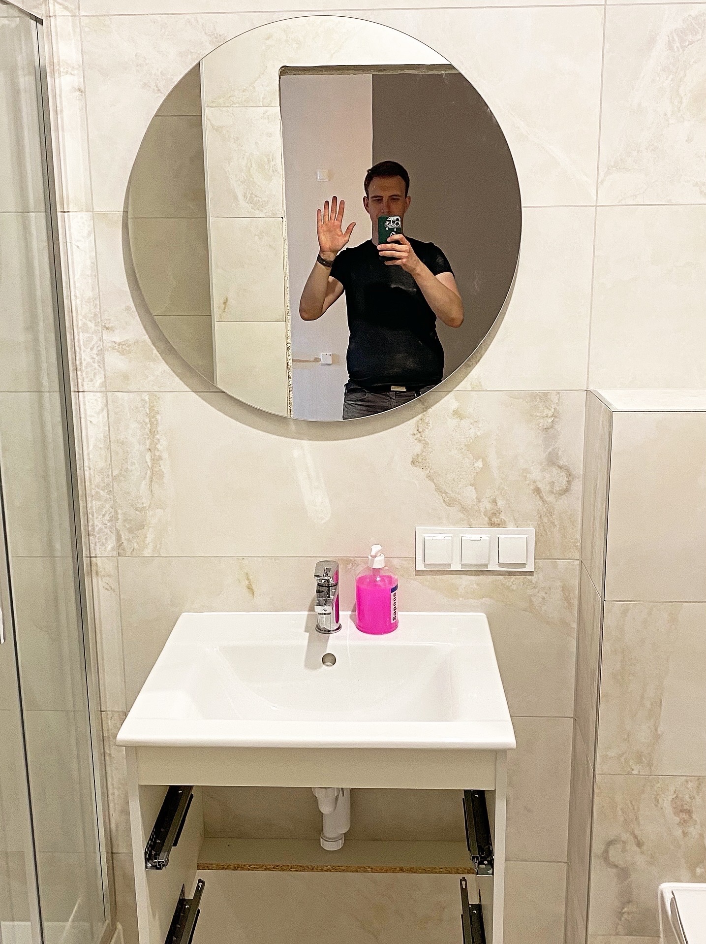 Wykończona łazienka z umywalką i lustrem, na ścianach płytki imitujące marmur. W lustrze odbija się osoba robiąca zdjęcie.