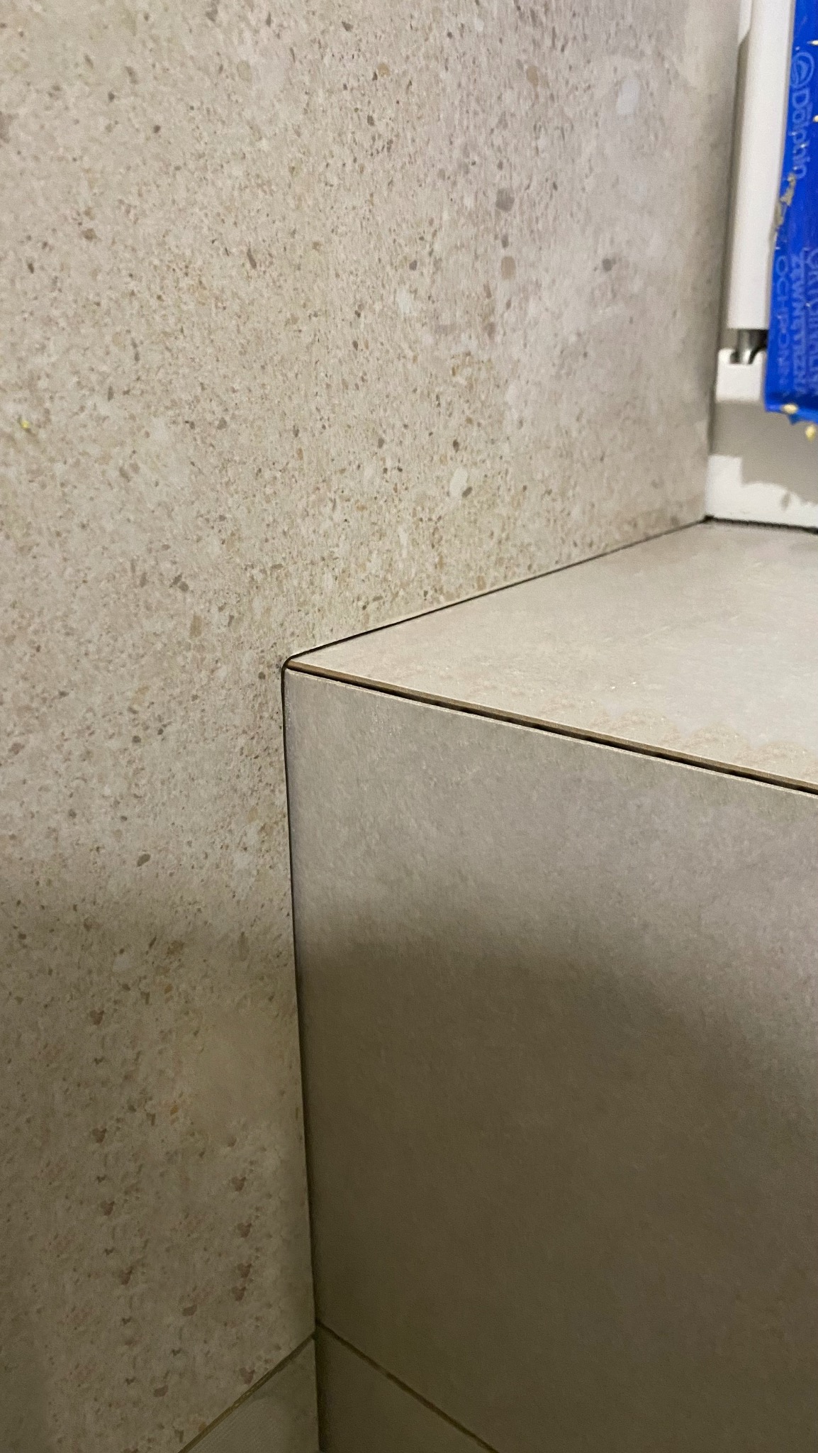 Beżowa ściana i zabudowa z płytek imitujących kamień, z widocznymi fugami, prezentująca precyzję wykonania w wykończeniu łazienki.