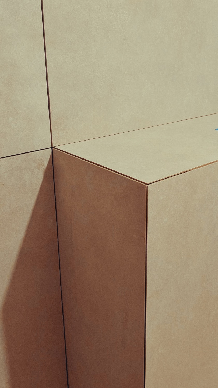 Detal wykończenia: narożnik obłożony beżowymi płytkami, z widocznymi fugami. Ujęcie z bliska, podkreślające precyzję wykonania i fakturę materiału.