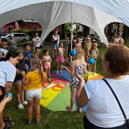 Art of Mind Norbert Ogoniak - Grupa dzieci i dorosłych pod białym namiotem, uczestniczących w warsztatach żonglerskich z kolorowymi piłkami i rekwizytami cyrkowymi, rozłożonymi na kolorowej macie.