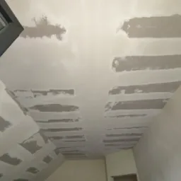 Sufit pod skosem w trakcie prac wykończeniowych, widoczne łączenia płyt gipsowo-kartonowych zaszpachlowane w pasy, przygotowane do dalszej obróbki.