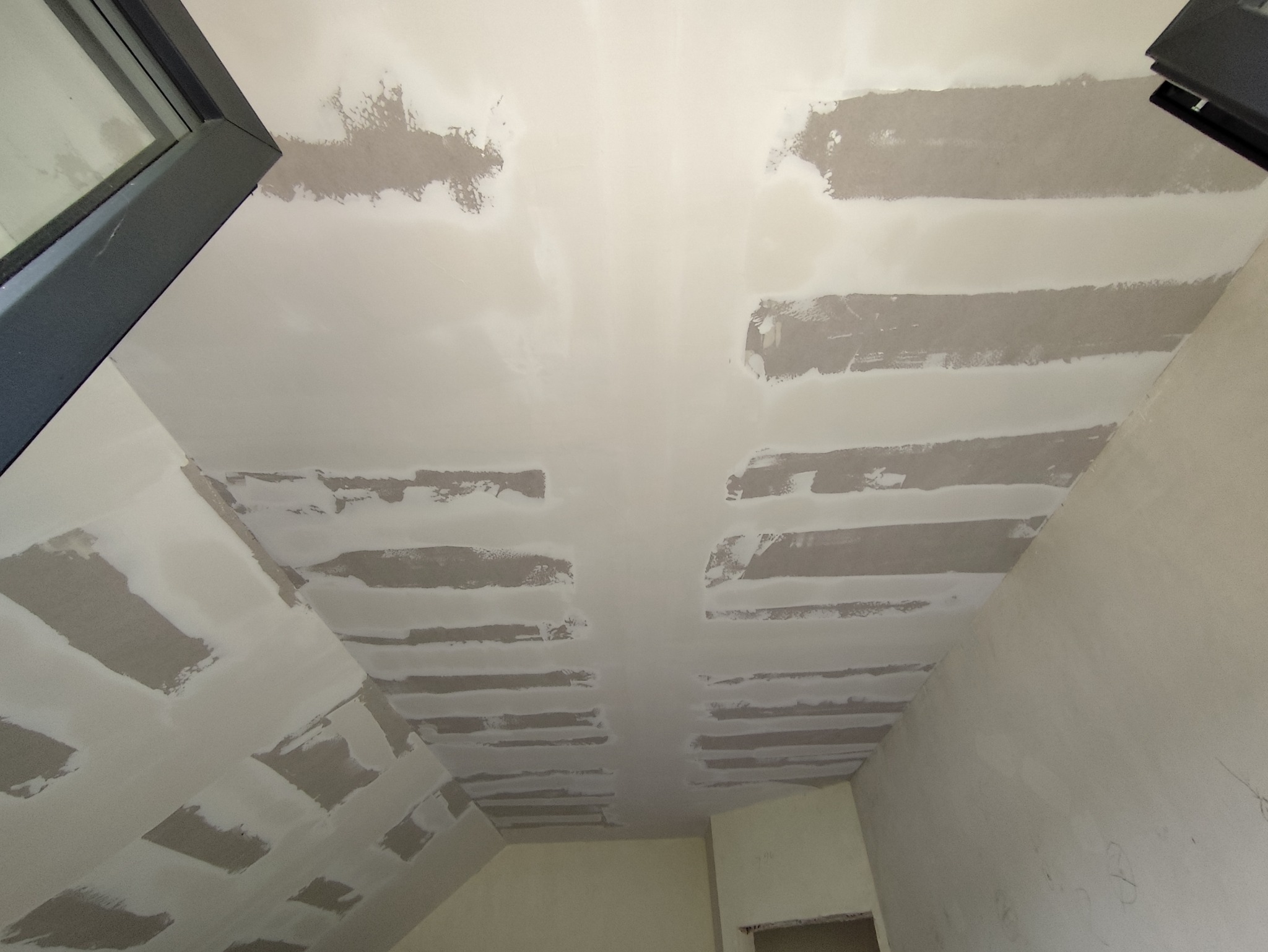 Sufit pod skosem w trakcie prac wykończeniowych, widoczne łączenia płyt gipsowo-kartonowych zaszpachlowane w pasy, przygotowane do dalszej obróbki.