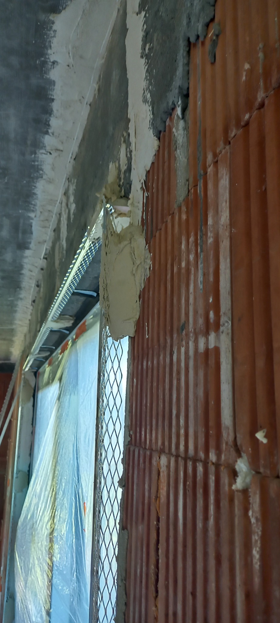 Aplikacja zaprawy na mur z pustaków ceramicznych Ytong, widoczna siatka wzmacniająca przy oknie, ślady wcześniejszych prac na suficie.