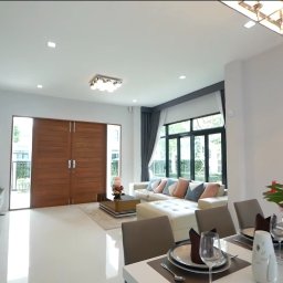 ELITE CLEAN Joanna Ziemiakowska - Jasne wnętrze domu po sprzątaniu: białe ściany i podłogi, stół z zastawą, sofa z poduszkami, drewniane drzwi. Widoczny znak firmy sprzątającej.