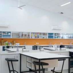 ELITE CLEAN Joanna Ziemiakowska - Wnętrze czystej, jasnej pracowni chemicznej z białymi blatami, czarnymi stołkami i pomarańczową mozaiką. Na ścianie logo firmy sprzątającej.