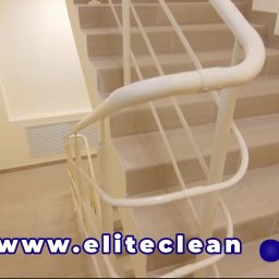 ELITE CLEAN Joanna Ziemiakowska - Klatka schodowa z beżowymi płytkami i białą balustradą, widok z góry. Czyste schody i ściany. Na dole widoczny adres strony internetowej firmy sprzątającej.