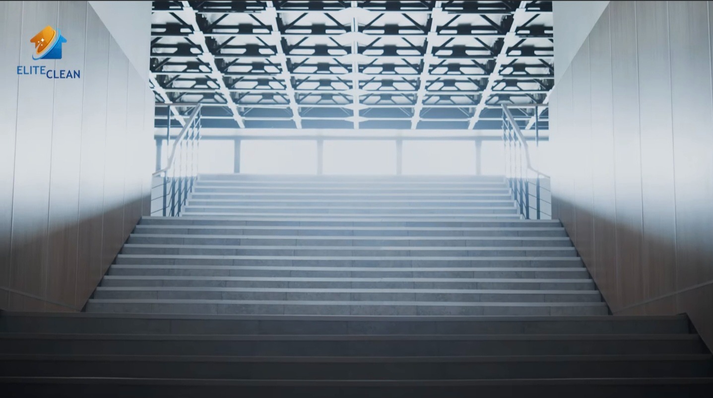 Schody w nowoczesnym biurowcu, widok z dołu, oświetlone światłem dziennym, z logo firmy sprzątającej Elite Clean w lewym górnym rogu.