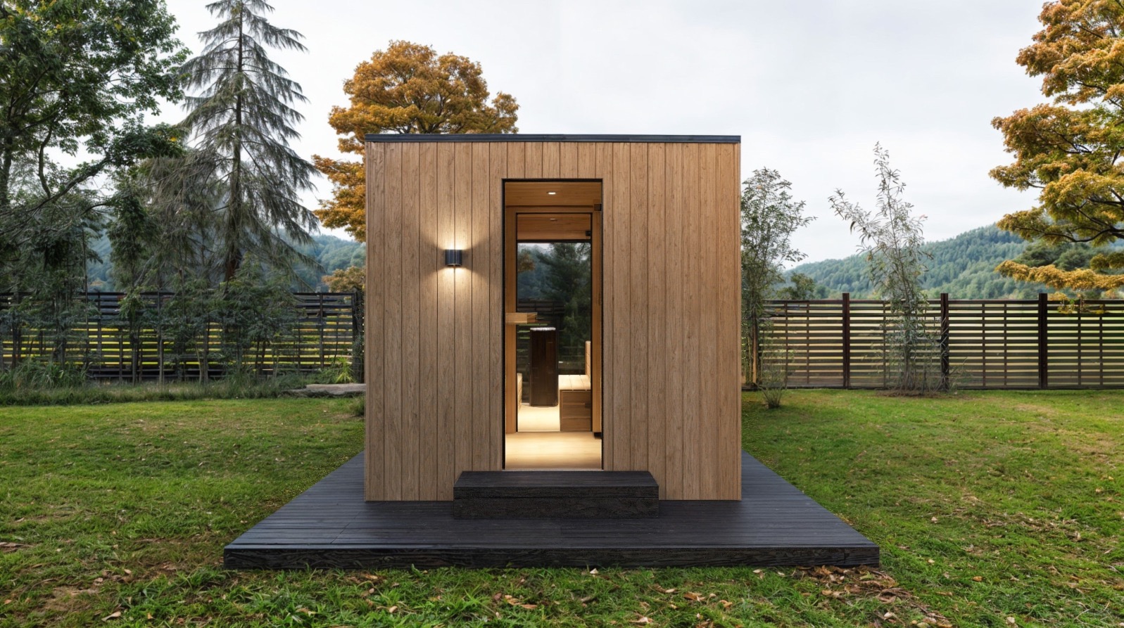 Nowoczesna sauna zewnętrzna z drewnianą elewacją, oświetleniem punktowym i czarnym tarasem, na tle zielonego trawnika i drewnianego ogrodzenia.