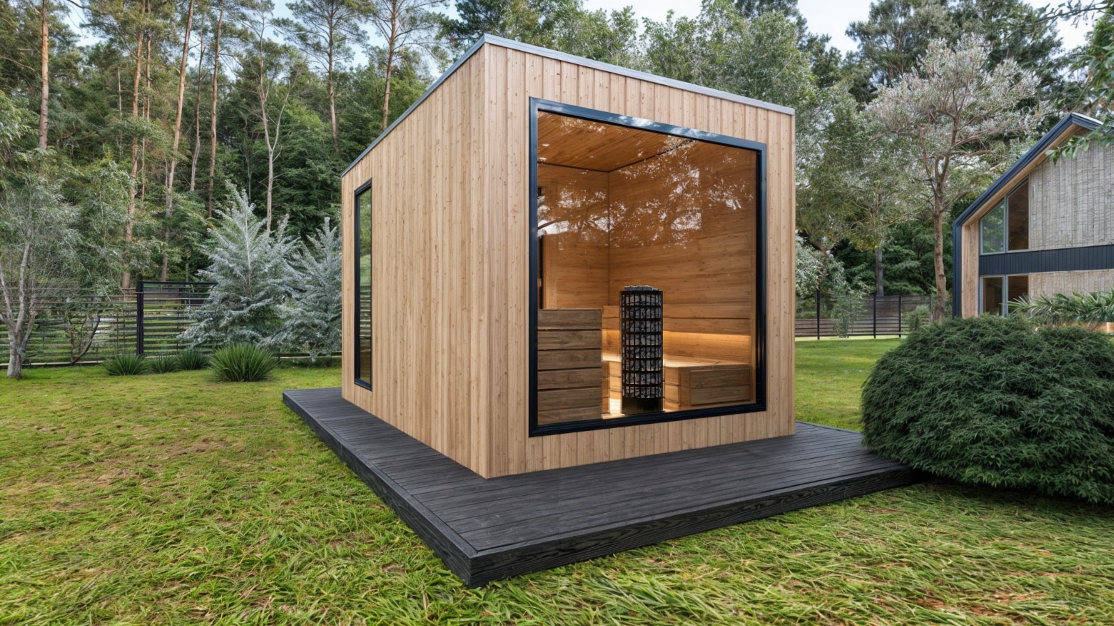 Nowoczesna, drewniana kabina z dużym oknem, ukazująca wnętrze z piecem i ławkami, umieszczona na ciemnoszarym podeście na trawniku, otoczona zielenią.
