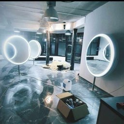 KAMA - Montaż oświetlonych okrągłych luster w pomieszczeniu z marmurową podłogą, widoczne materiały budowlane i narzędzia w kartonie.