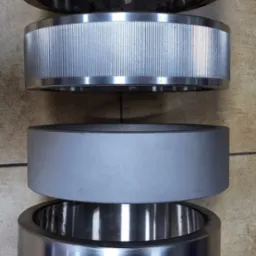 Cztery metalowe pierścienie o różnej fakturze i wykończeniu, ułożone jeden na drugim: radełkowany, żebrowany, gładki szary i polerowany na wysoki połysk.