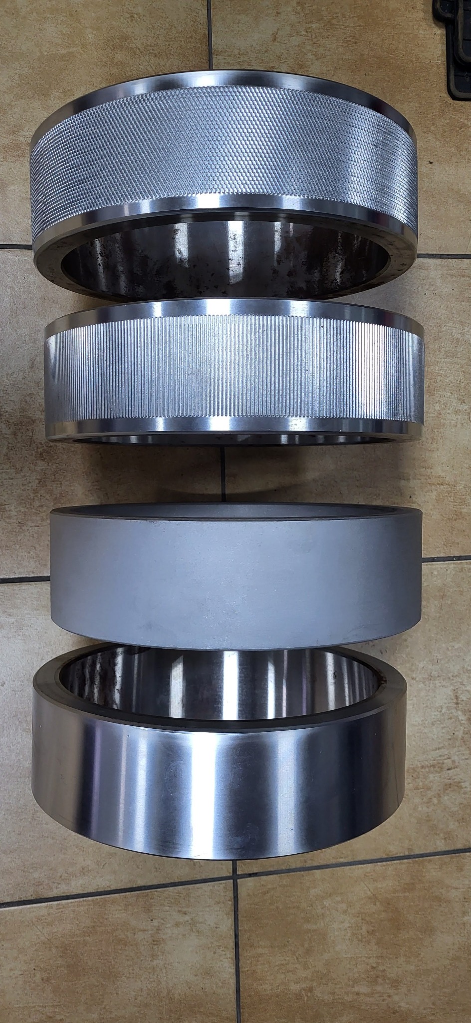 Cztery metalowe pierścienie o różnej fakturze i wykończeniu, ułożone jeden na drugim: radełkowany, żebrowany, gładki szary i polerowany na wysoki połysk.