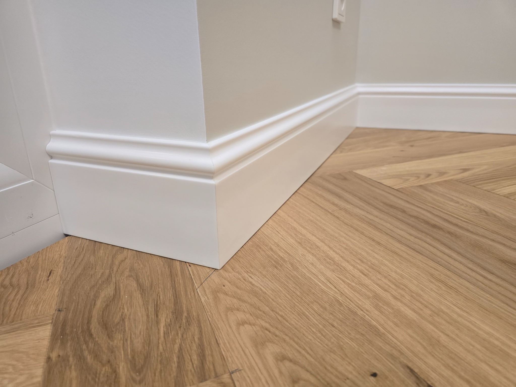 Ułożony parkiet w jodełkę francuską z białą listwą przypodłogową i narożnikiem, widok z niskiej perspektywy.