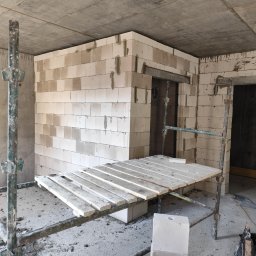 Topolowa 2C - Wnętrze w trakcie budowy w Miłobądzu: widok na wznoszone ściany z białych bloczków, częściowo osadzone nadproża drzwiowe, z widocznym rusztowaniem i workiem zaprawy na podłodze.